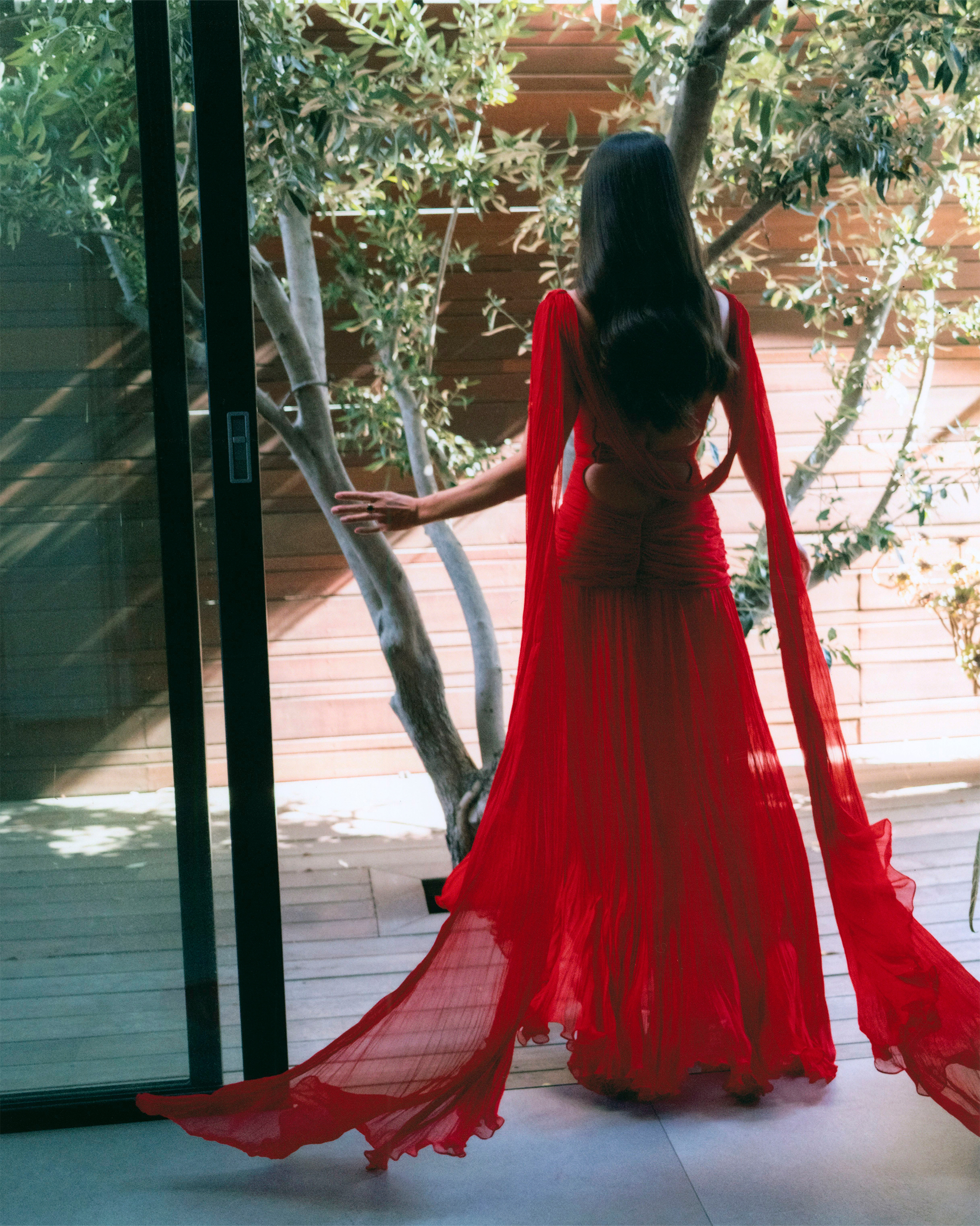 Sara Sampaio in her final look before the Superman Los Angeles premiere. She is turned away from the camera wearing a red Marmar Halim gown.