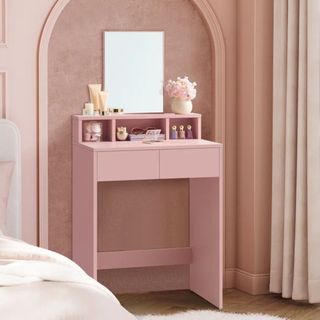 A slim pink dressing table with a mirror against a lighter pink wall