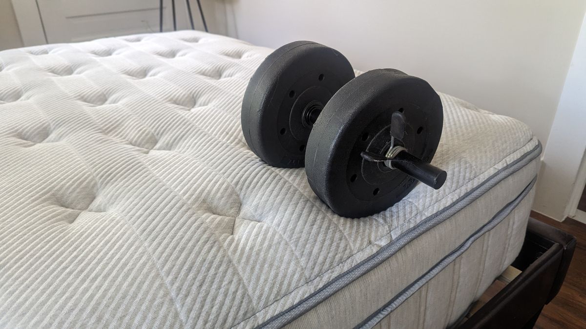 Edge control test for the Leesa Oasis Chill Hybrid mattress review shows a large black weight placed near a wine glass on the surface of the Leesa Oasis Chill Hybrid shows a heavy black weight placed right on the edge of the mattress but it doesn't sag at all