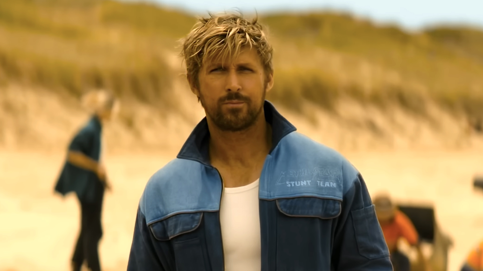Ryan Gosling, blonde hair and baby blue and navy stunt team jacket with collar popped, in The Fall Guy (2024).