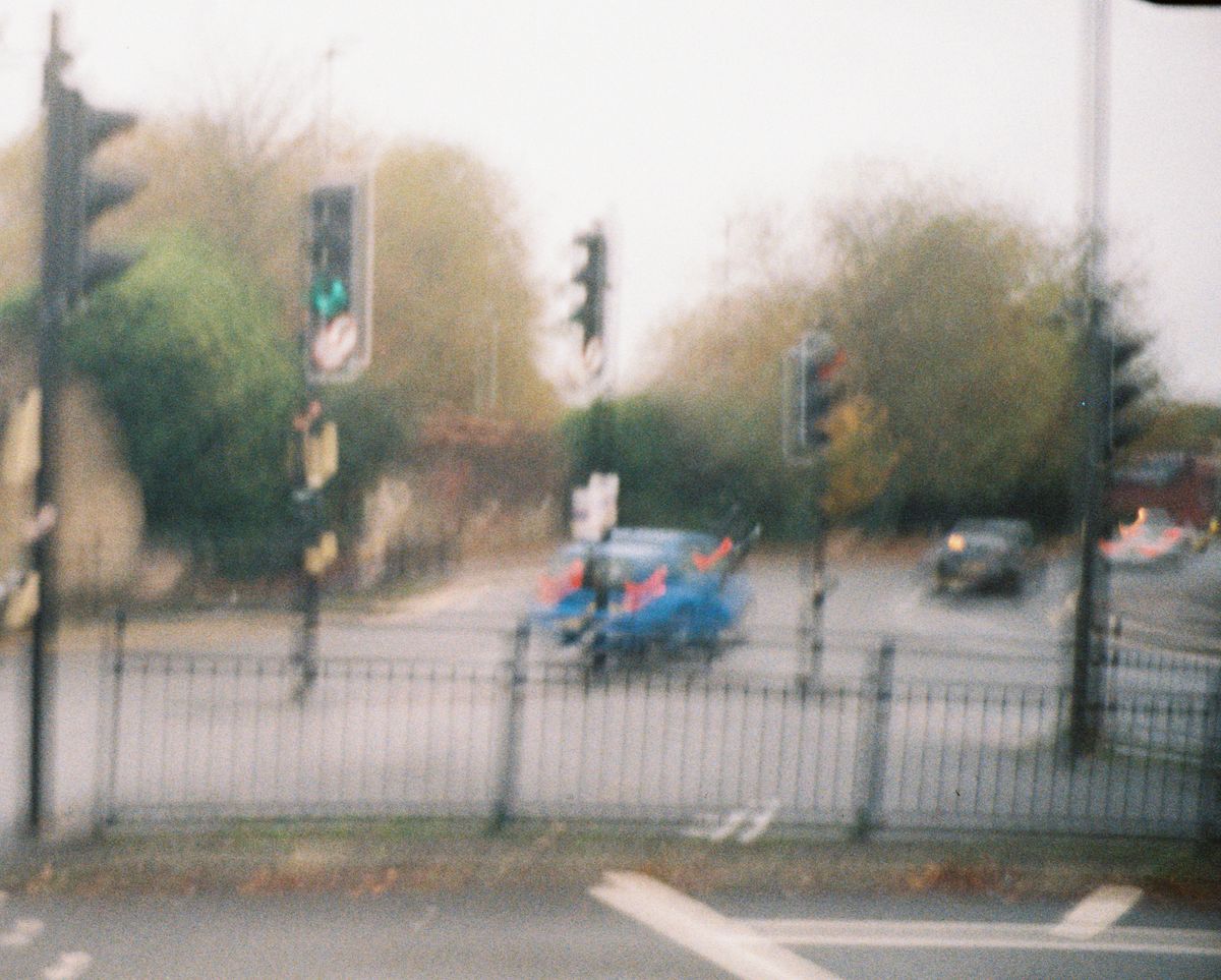 A blurry photo of a car, traffic lights and a road, taken on a Lomography Lomomatic 110 film camera