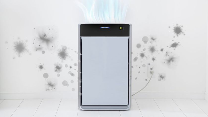 A modern air purifier placed against a white wall and plugged into a nearby socket. Grey particle graphics surround it, showing the removal of dust and allergens.
