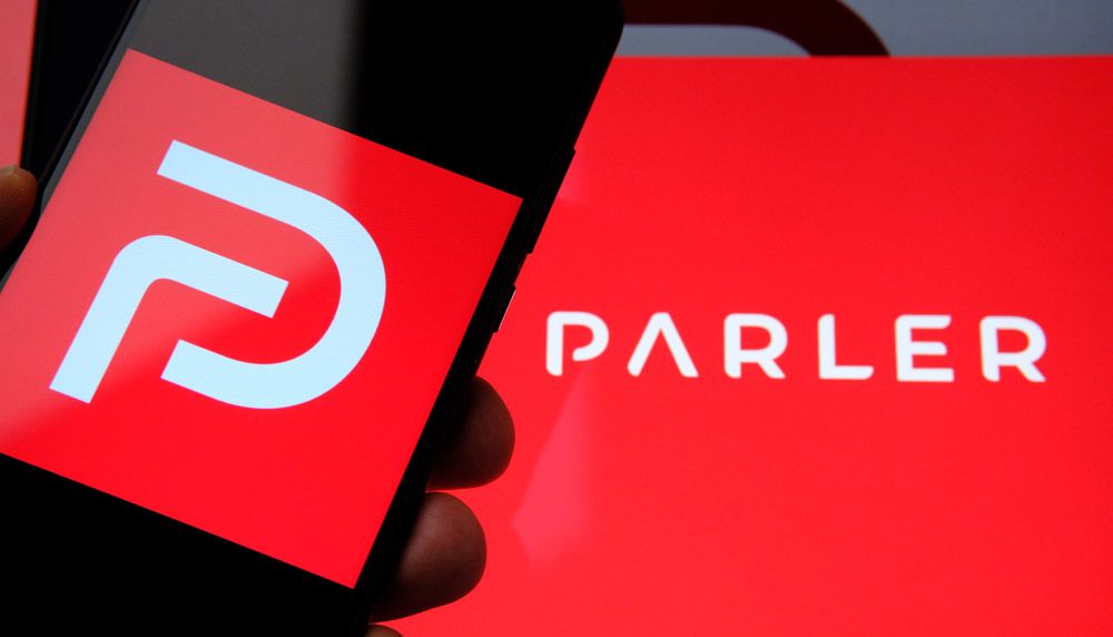 The Parler app&#039;s logo displayed on a smartphone screen and what might be a PC.