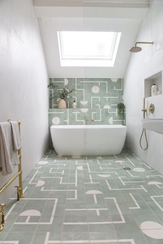 geometric green floor and wall tiles in bathroom with wet room, white tub
