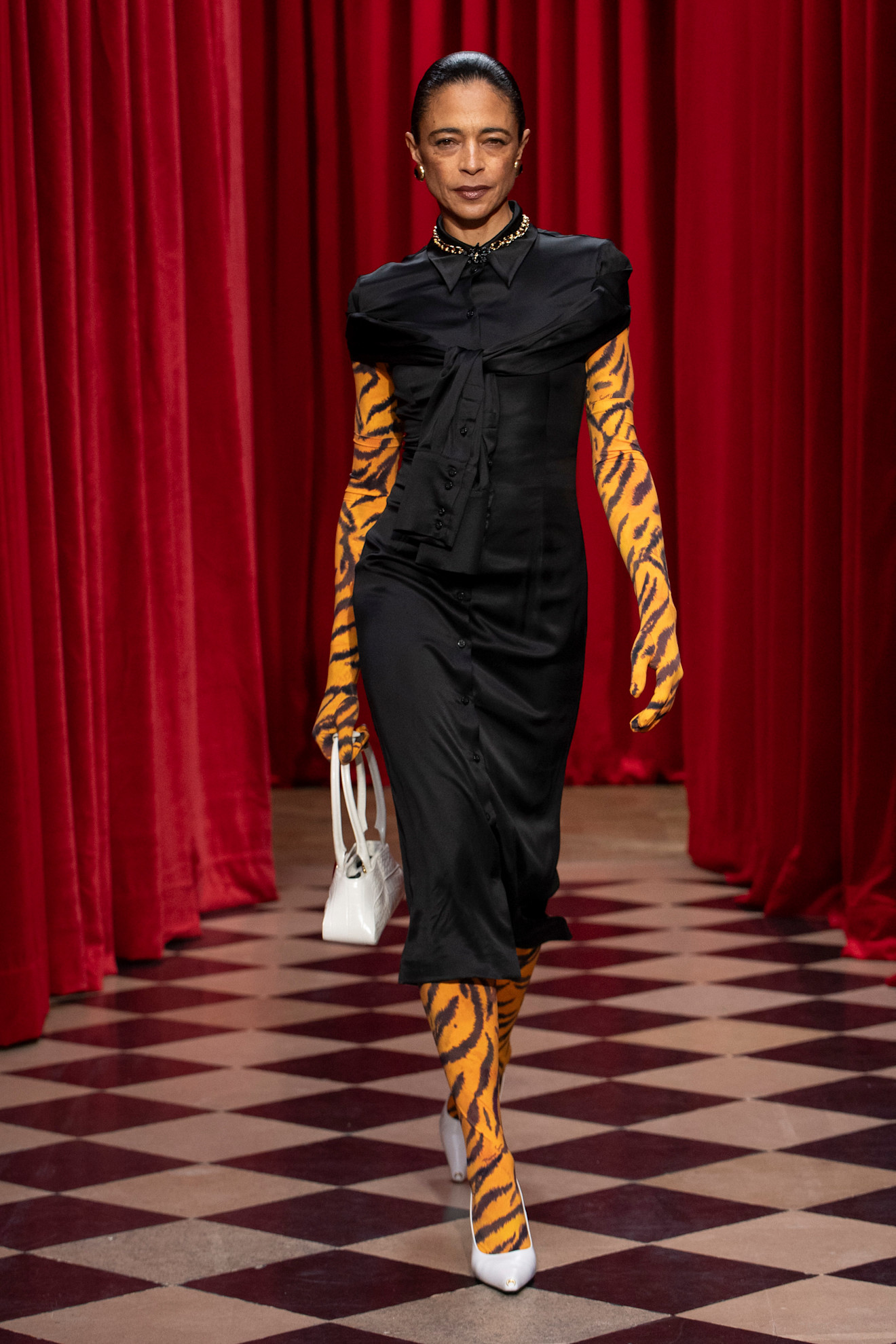 A model wearing a black top and skirt with orange tiger print gloves and tights at Marine Serre Fall 2025