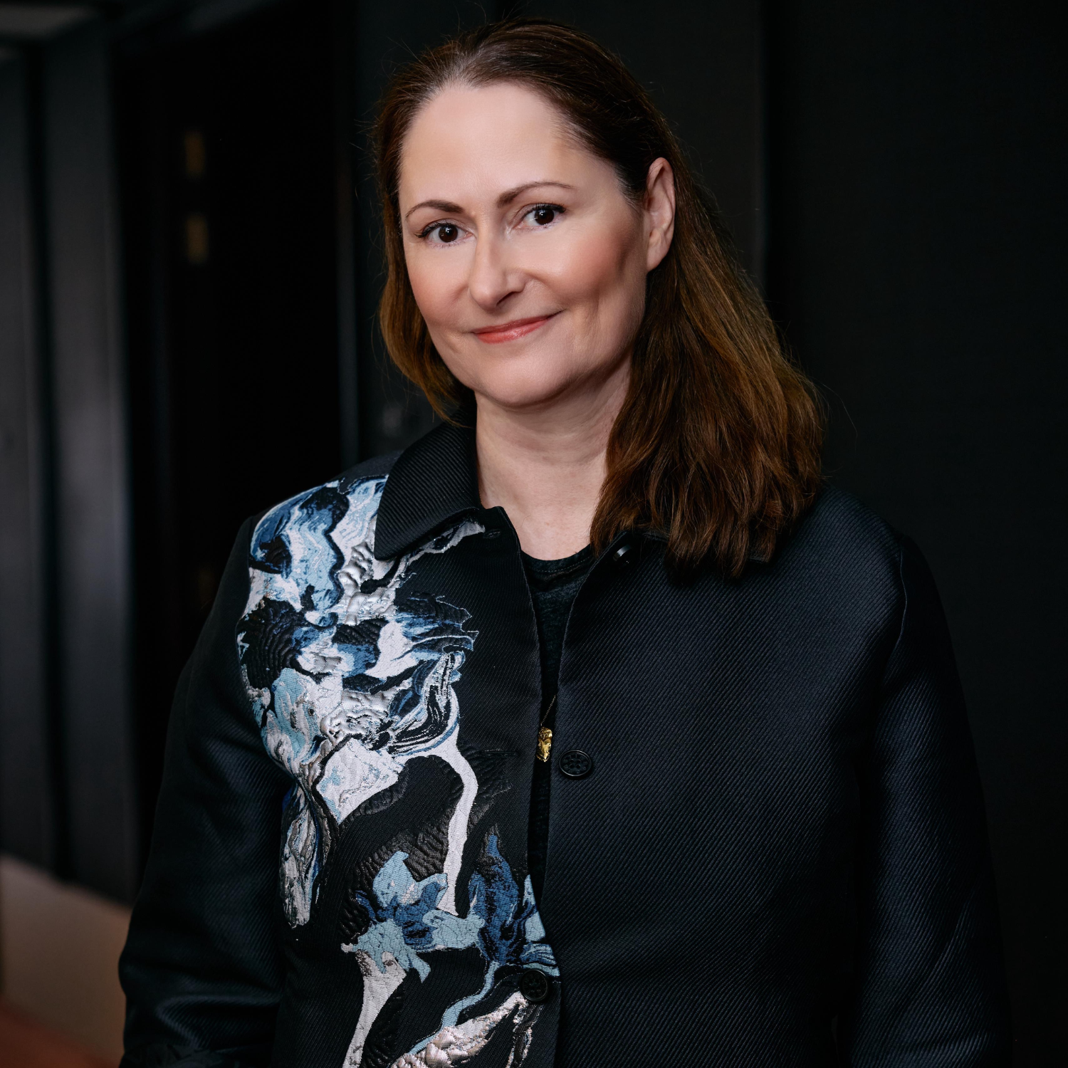 A picture of a woman with short brown hair in a dark patterned jacket