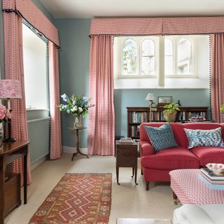 A living room in a traditional home with blue walls and red patterned curtains and upholstery