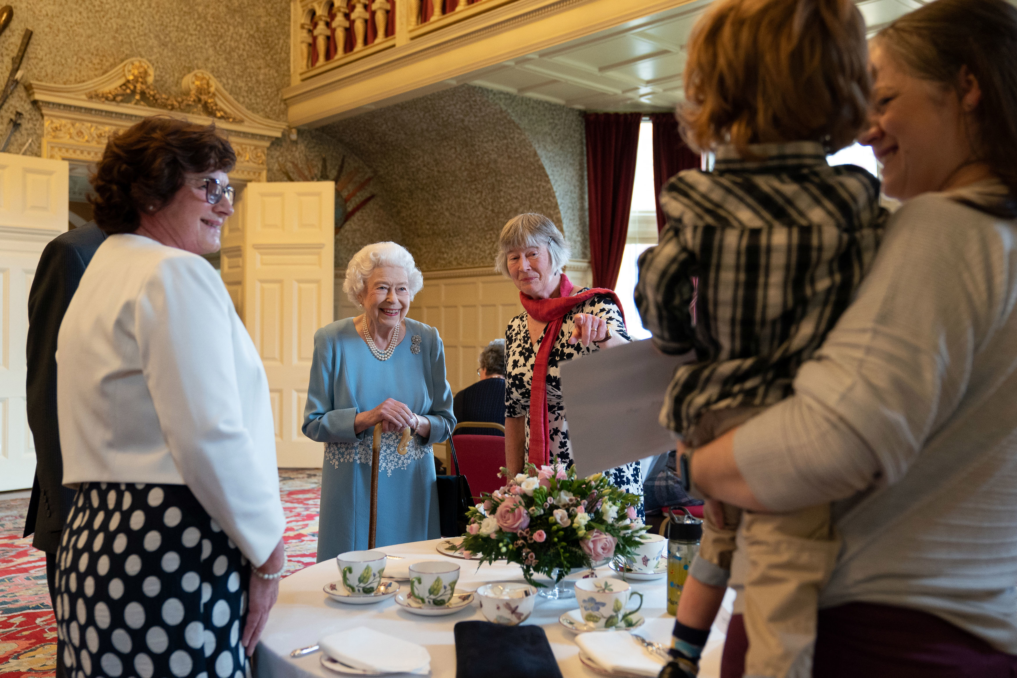 Queen Elizabeth smiling in front of a table with teacups and flowers