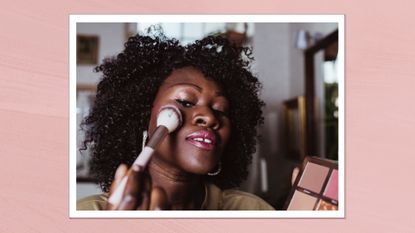 A close-up of a woman with curly hair, applying blush with a brush to the apples of her cheeks/ in a pink template