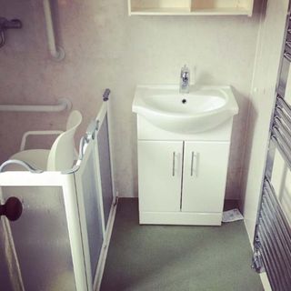 Plain bathroom with a white bathroom sink next to a washing corner with a chair and handrail