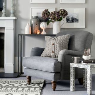 Grey armchair with textured cushion in a grey living room by a picture wall