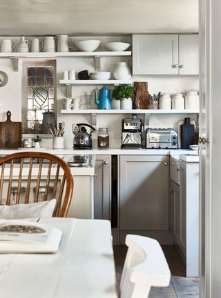 cottage kitchen with grey cabinets and open shelves and white table with white and windsor style chairs