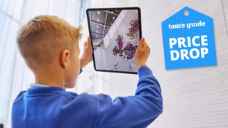 Child holding iPad with image on screen and Tom&#039;s Guide Price drop deal badge in top right corner