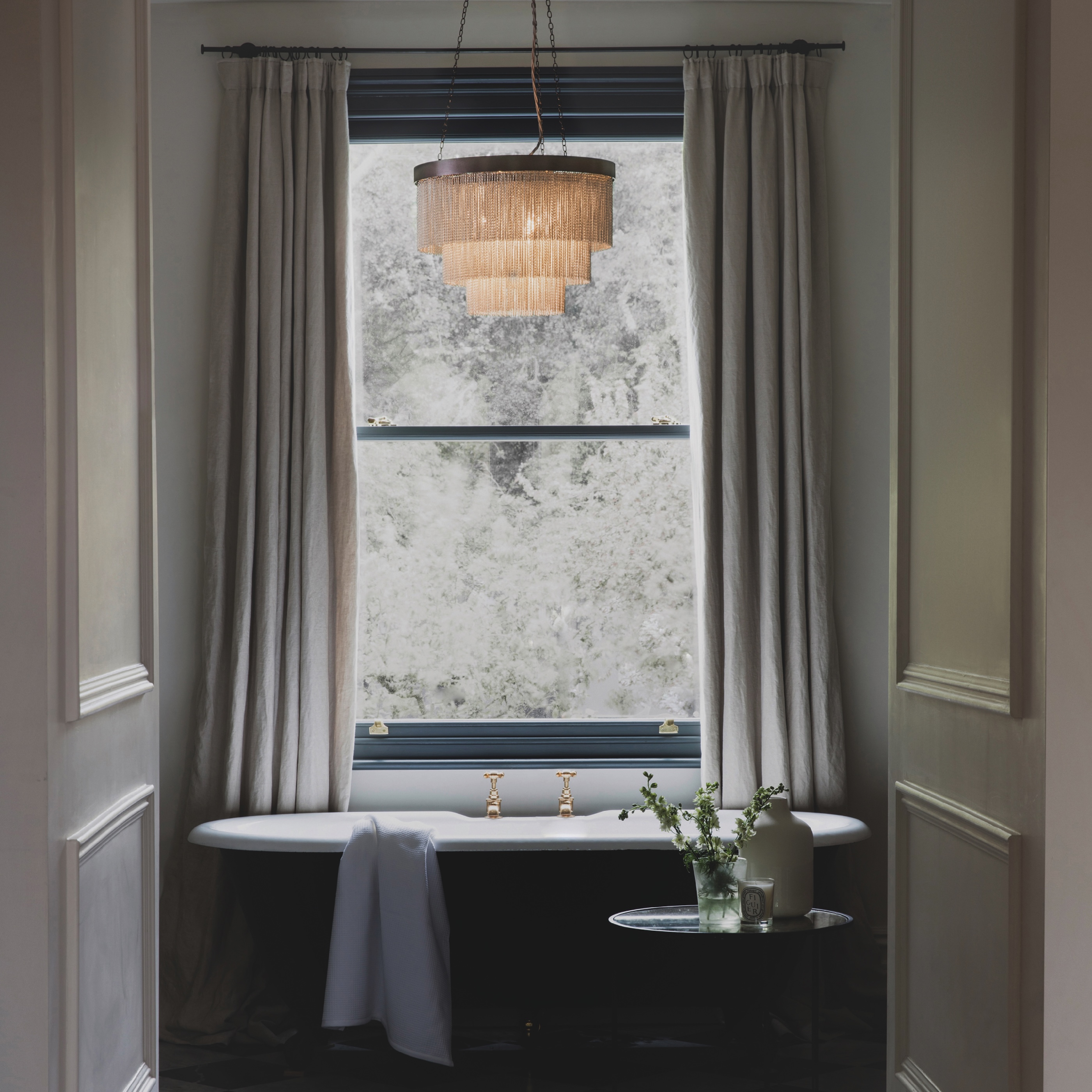 A chandelier above a centralised bath in front of a window