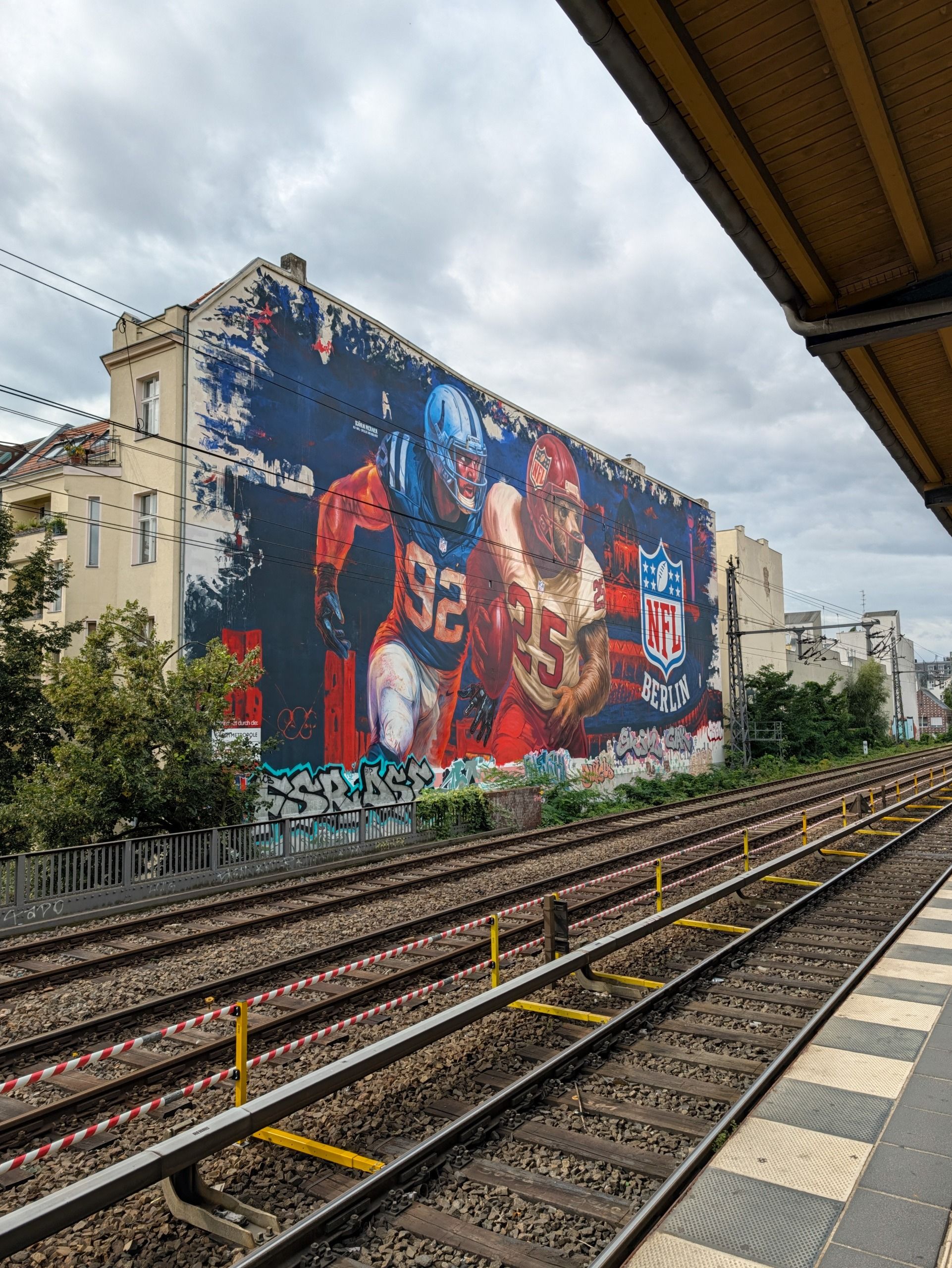 Large NFL Berlin mural of two American football players beside railway tracks.