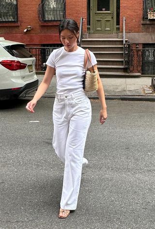 a woman's outfit showing what to wear in 80-degree weather with a white t-shirt styled with white jeans and a raffia tote bag and tan sandals