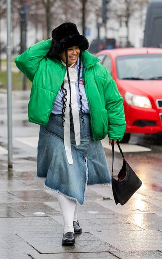 woman in denim midi skirt, white top, and green jacket