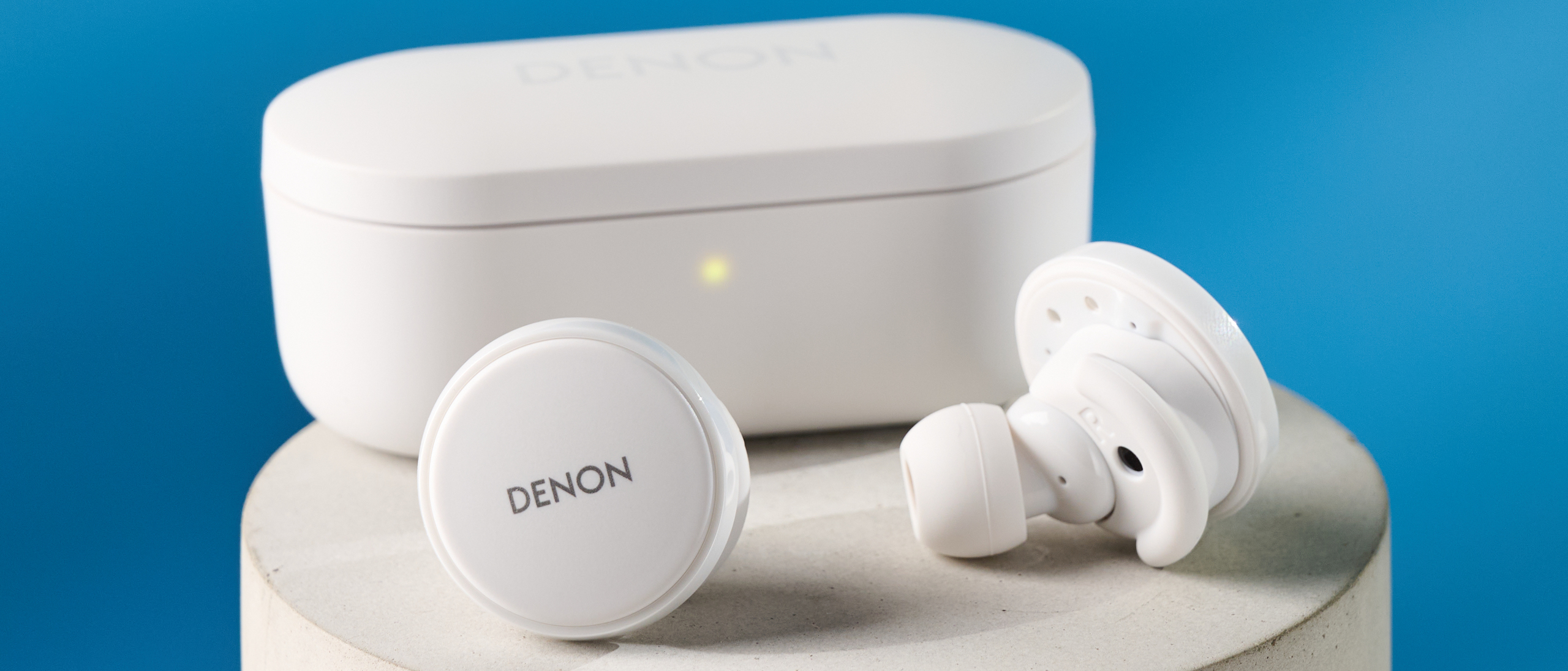 the denon perL Pro wireless earbuds in white, with circular earbud shapes, and a white charging case, photographed against a blue background