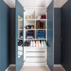 Blue wardrobes in a blue room with the doors open, showing drawers and shelves filled with clothes and shoes