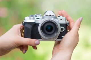 A person holding an Olympus OM-D E-M10 Mark IV, one of the best cheap cameras