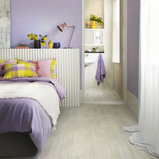 Bleached wood flooring in a purple bedroom with purple bedding on the bed and panelled headboard
