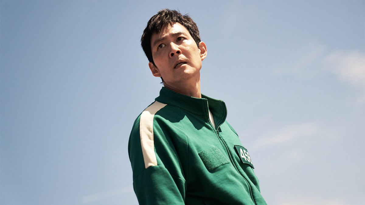 A man with a green jacket on looks over his shoulder slightly with a blue sky behind him