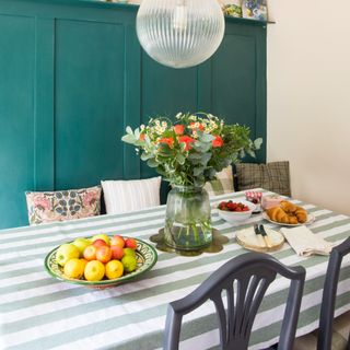 A dining table covered in a striped tablecloth with mismatched tableware and a vase of fresh flowers