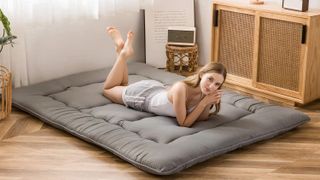A woman with brown hair lies on her stomach on a grey colour Japanese floor mattress
