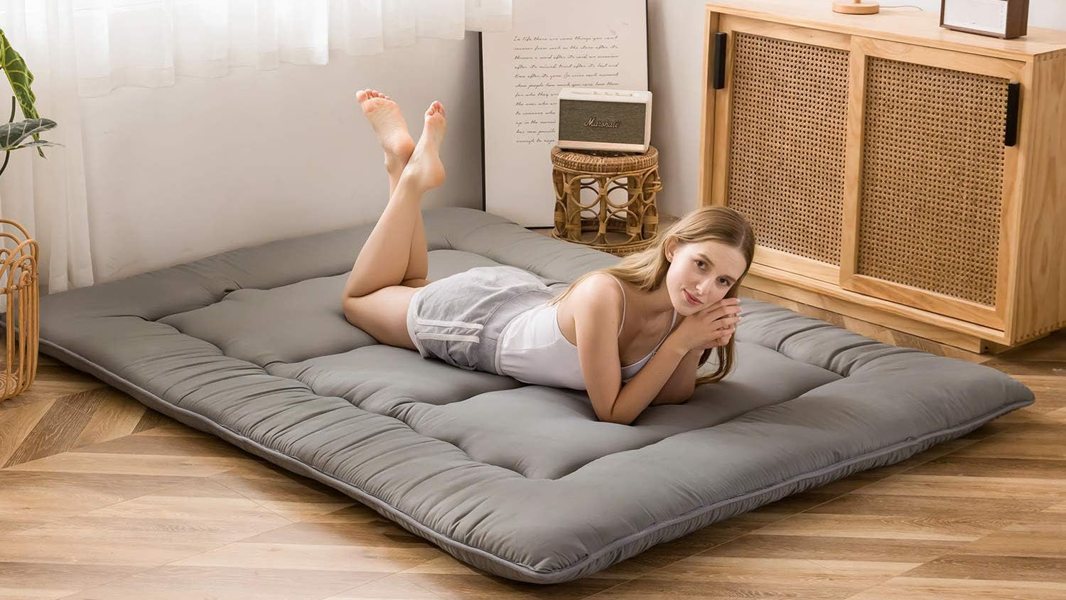 A woman with brown hair lies on her stomach on a grey colour Japanese floor mattress