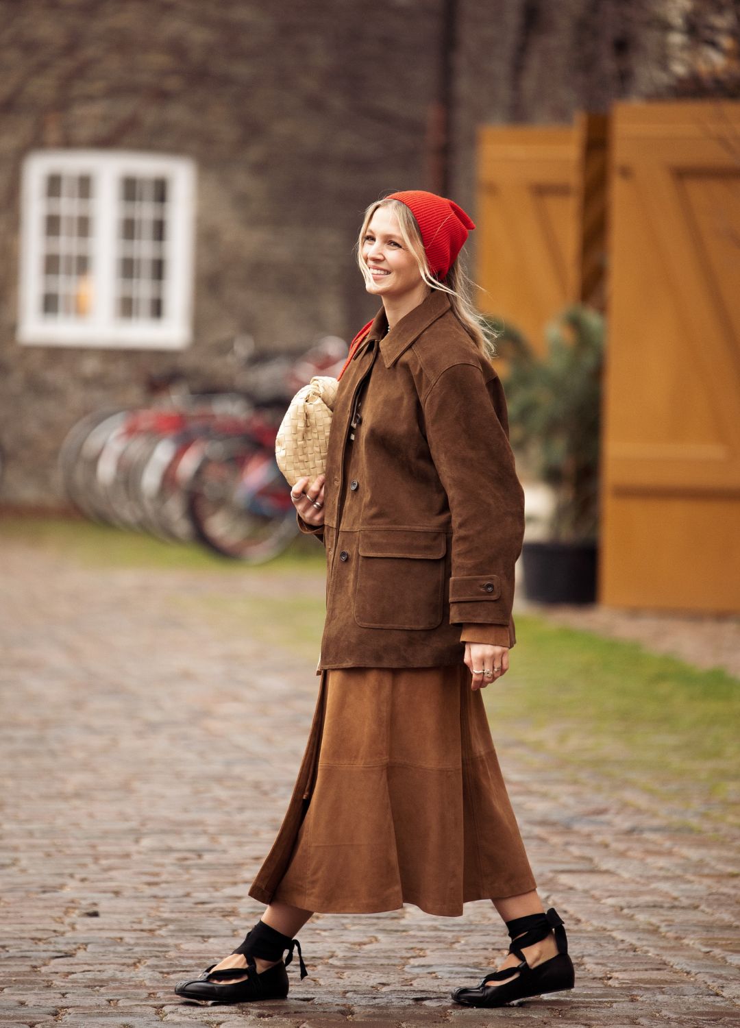 Hollie Mercedes Peters wears brown skirt, brown suede jacket, beige bag, red head scarf and black shoes outside the Munthe fashion show during the Copenhagen Fashion Week Autumn/Winter 2025 on January 30, 2025 in Copenhagen, Denmark