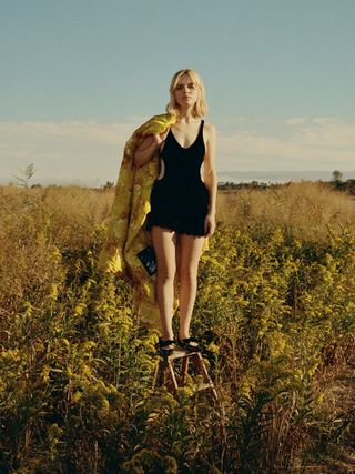 Odessa Young wears a black jumpsuit among a field of yellow flowers.