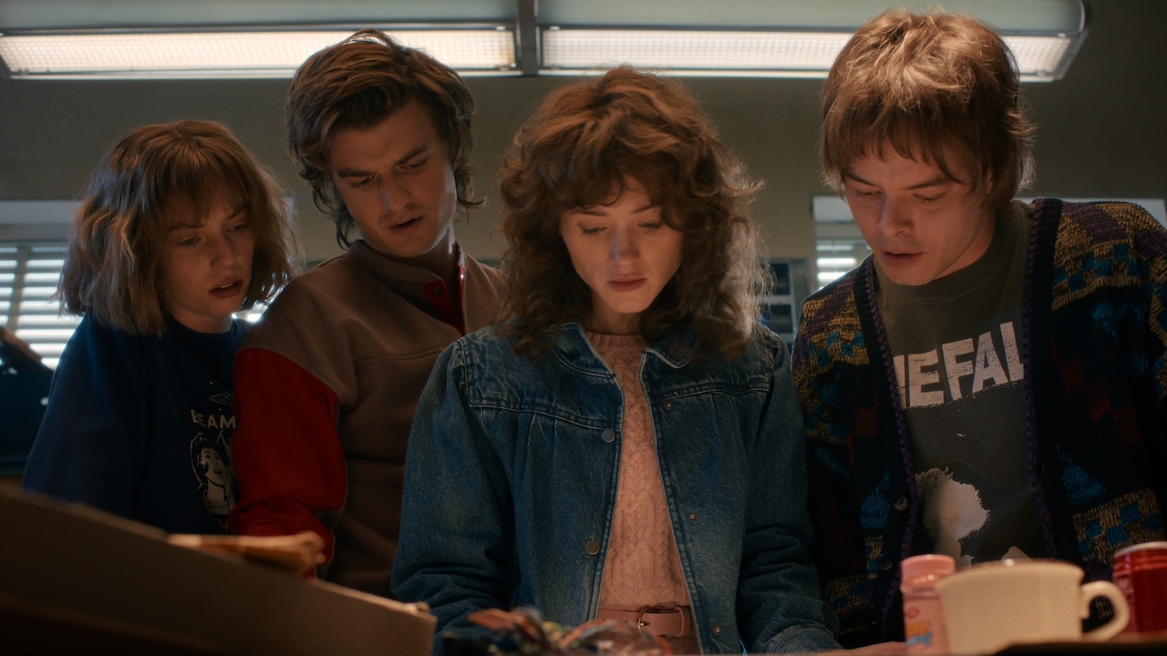 Robin, Steve, Nancy and Jonathan looking down at something in the Hawkins radio station in Stranger Things