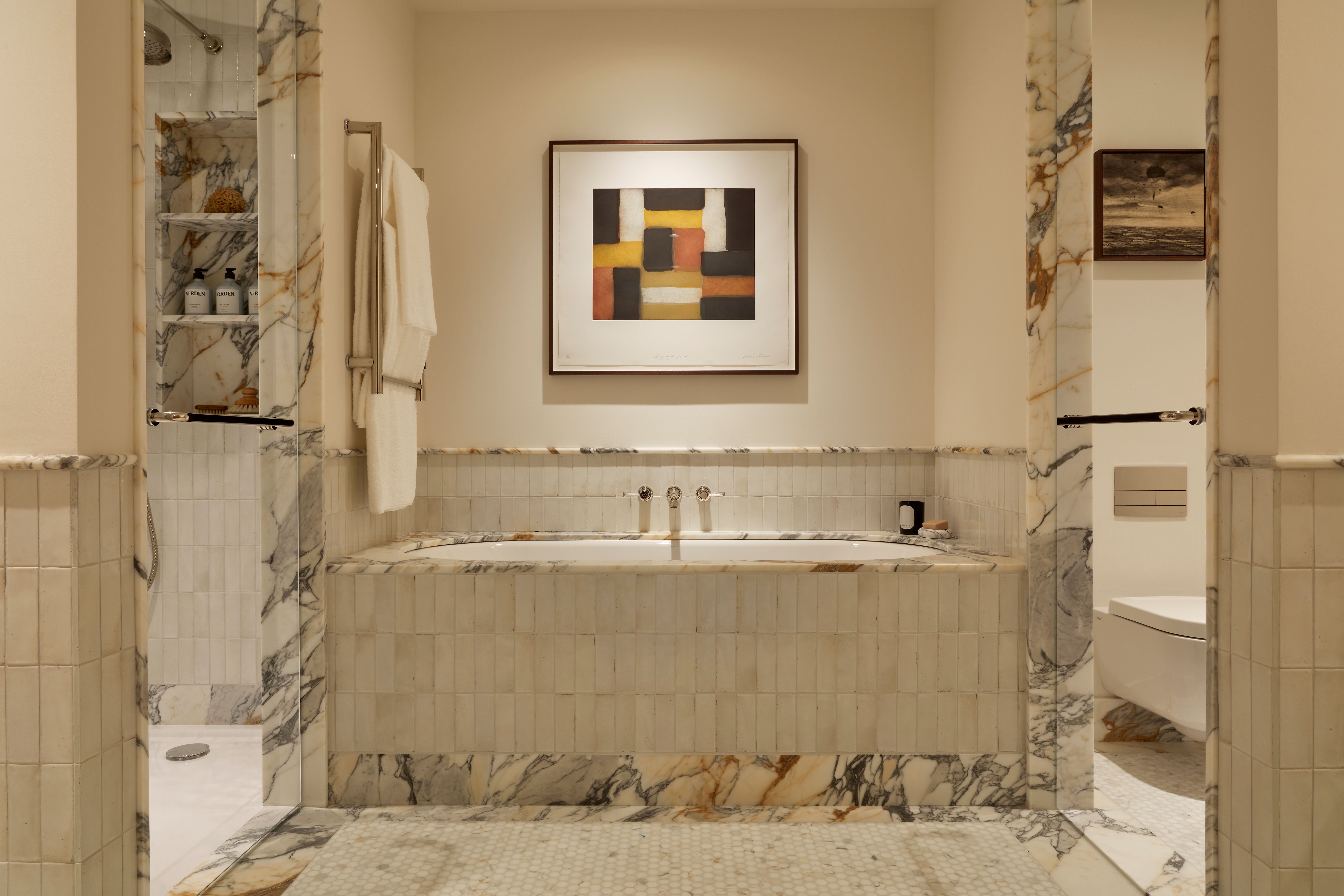 a luxury bathroom with a built-in tub and a shower room on one side, and a toilet on the other. The doors and tub are framed in a marble trim