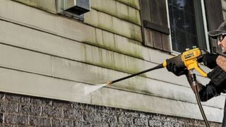 Man uses Dewalt cordless pressure washer on vinyl siding