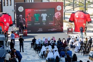 The four leaders' jerseys are presented to a crowd on a large screen on a sunny terrace