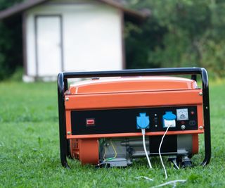 An orange and black portable generator outside on a short grass lawn