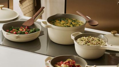 A set of cream colored cookware on a black glass stove top, full of a variety of foods
