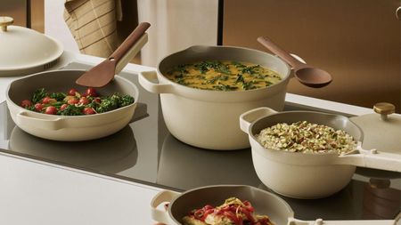 A set of cream colored cookware on a black glass stove top, full of a variety of foods