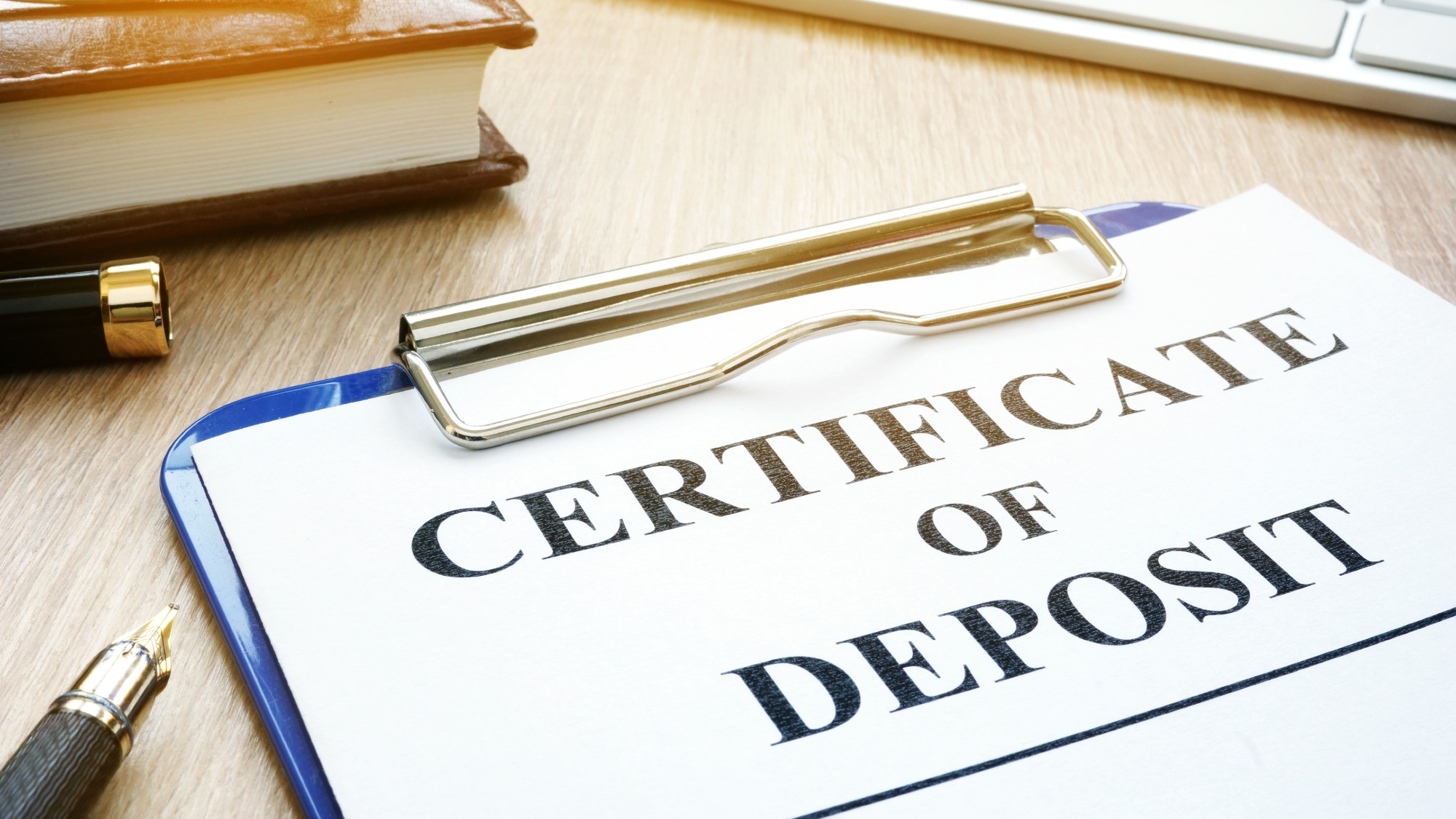 A clipboard holding a paper that reads "certificate of deposit and a pen sitting on a desk