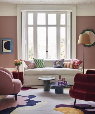 A pink painted living room with white sofa and colorful armchair and accessories.
