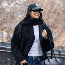 Amelia Gray wearing a Yankees baseball cap, black scarf and coat, white T-shirt, baggy jeans, and black glove flats