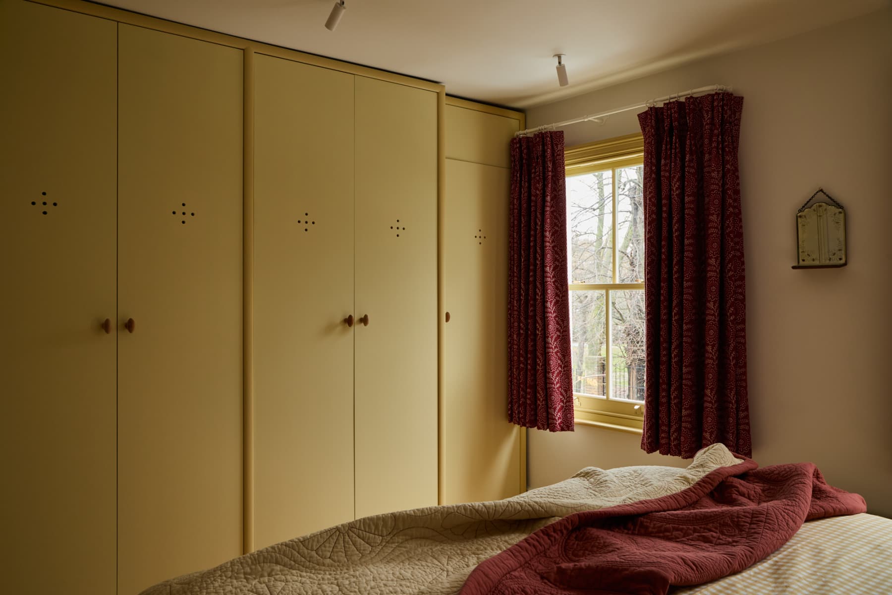 yellow bedroom with short red curtains, beige walls, and yellow bedspread with red blanket