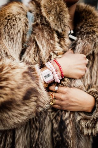 a guest at fashion month wears a fur coat with a watch and bracelets that may be impacted by president trump's tariffs