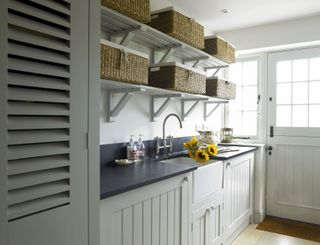 Neutral cupboards with a dark worktop and shelving with storage baskets