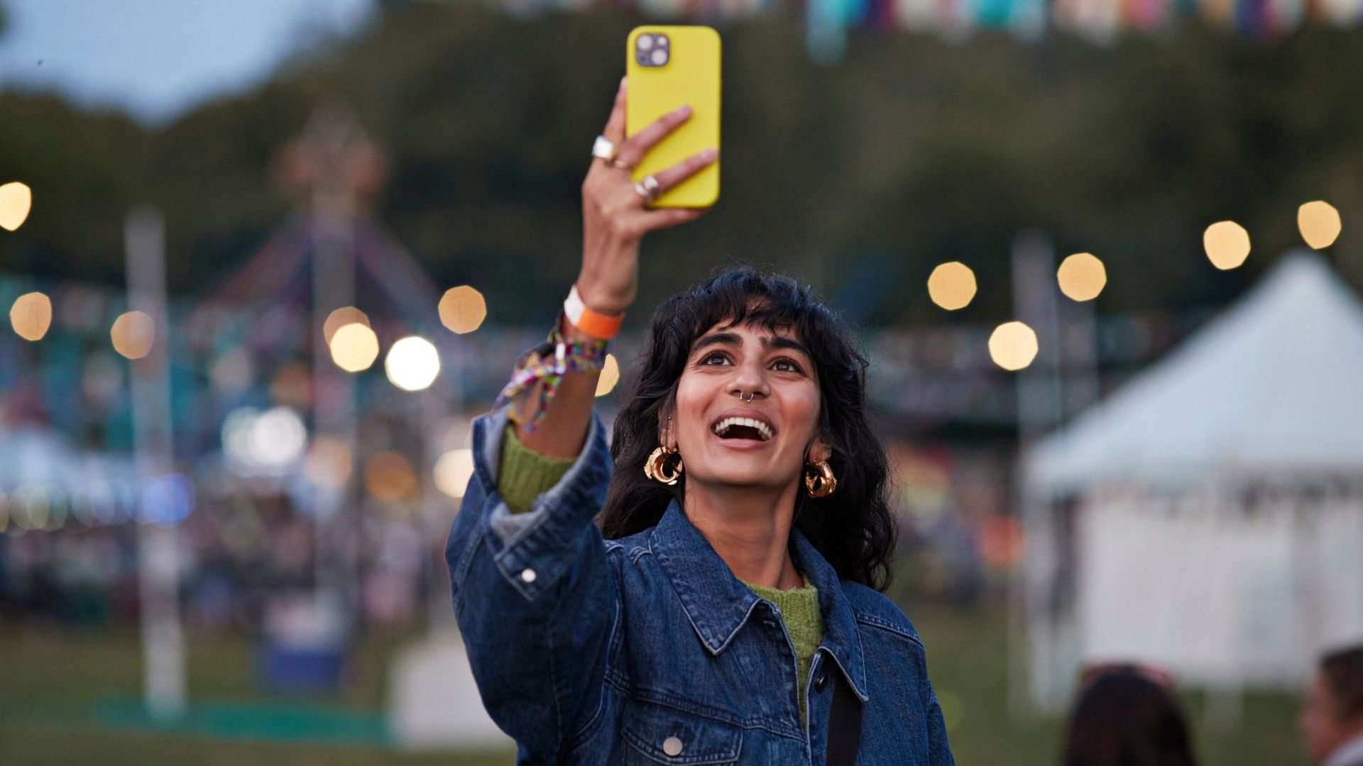 A person holding their phone at an outdoor festival.