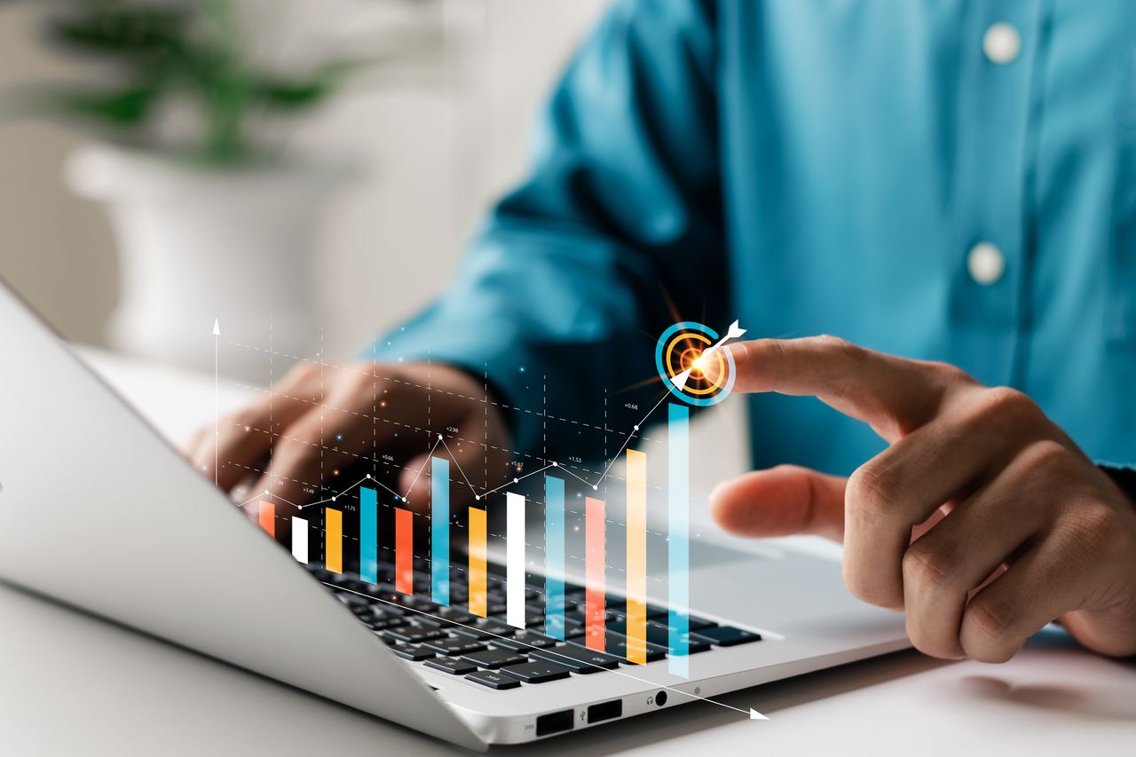 person looking at financial graphs on laptop with digital rendition of graph coming out of keyboard