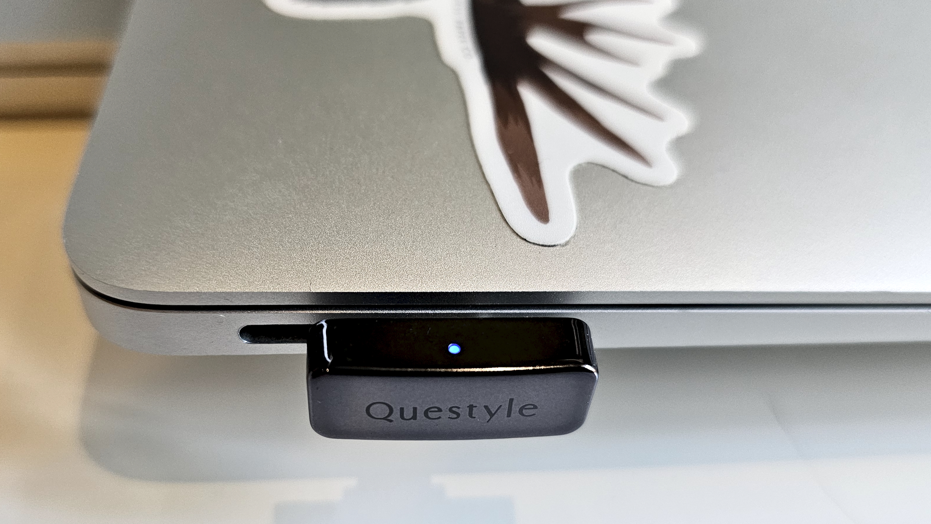The Questyle QCC Dongle Pro with a smartphone to denote size, on a light wooden table