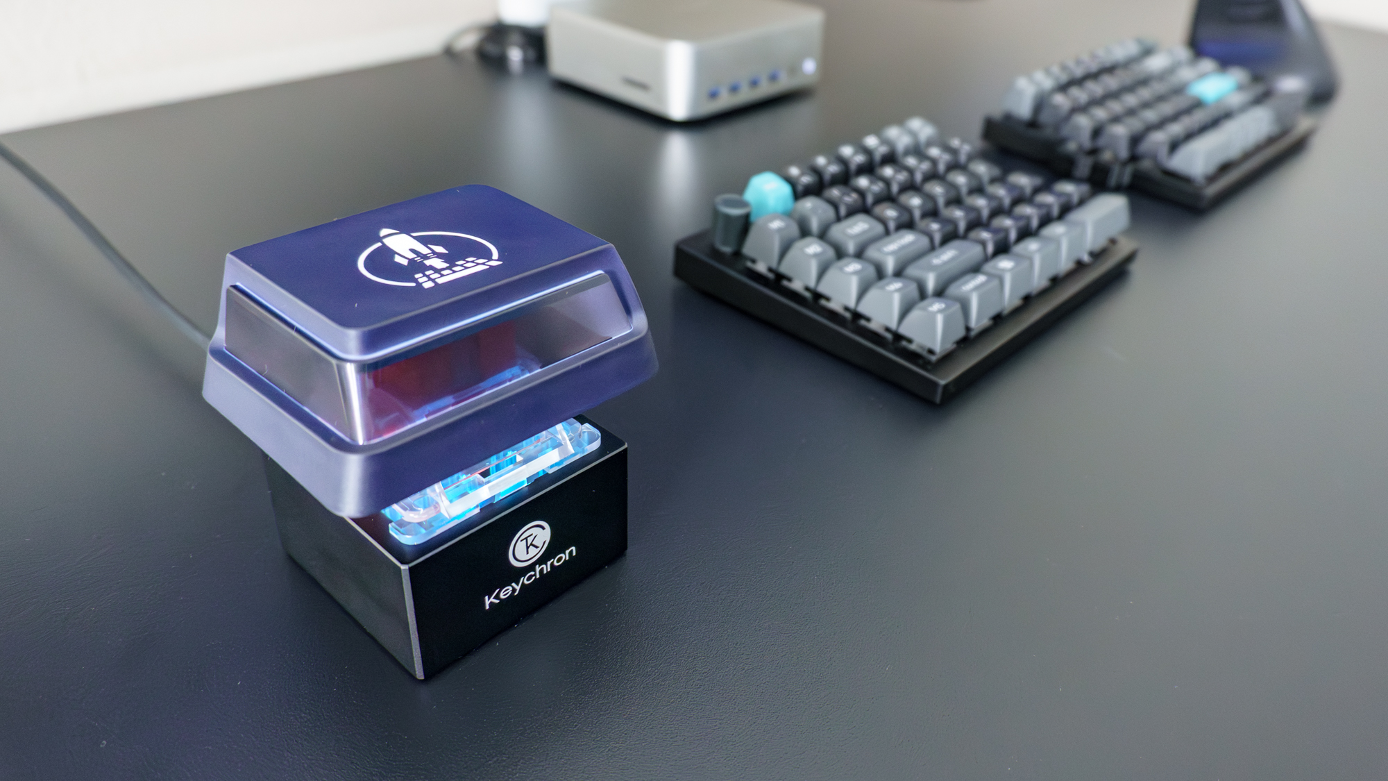 The Keychron Q0 Mini 8K Action Key next to a split mechanical keyboard on a desk
