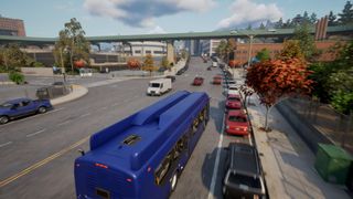 A blue bus travels down a busy city road with cars parked in bays to its right