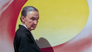 Photo of artist Georgia O'Keeffe stood in front of a bright yellow painting